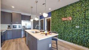 Une cuisine moderne avec des meubles de couleur sombre, un îlot central et un néon mural.