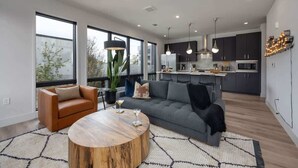Un salon moderne avec un canapé, une table basse et un coin repas, la cuisine étant visible à l’arrière-plan.