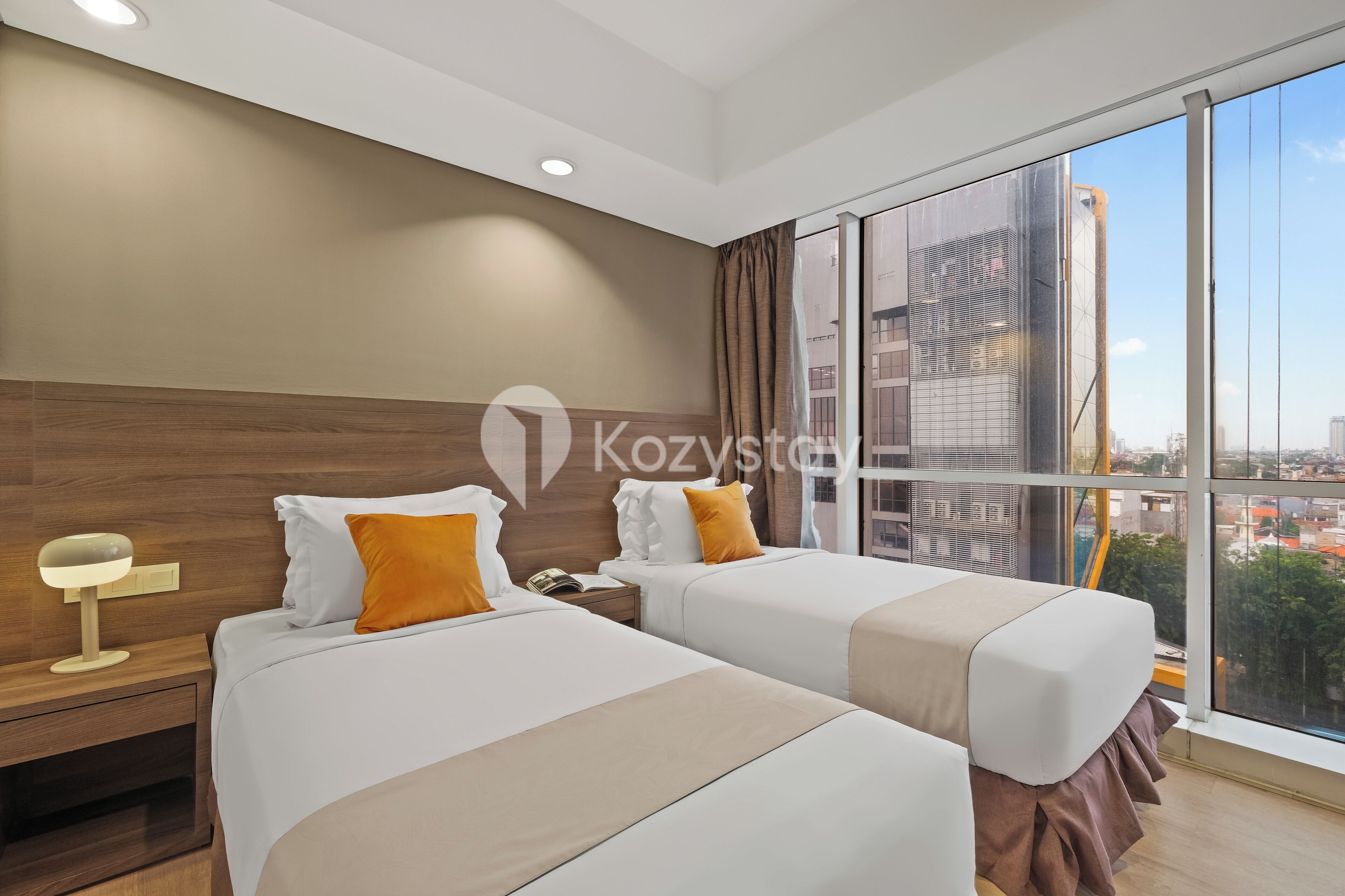A hotel room with two beds, a large window with a city view, and a nightstand with a lamp.