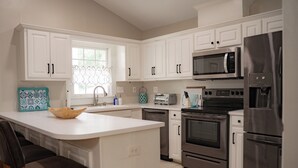 Una cocina moderna con armarios blancos, electrodomésticos de acero inoxidable, una isla central y un ventanal con cortina decorativa.