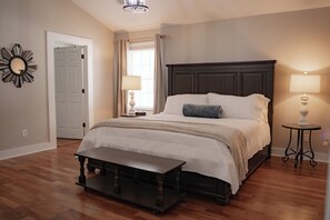 Une chambre à coucher avec un grand lit, une table de chevet, un banc, un miroir et une porte.