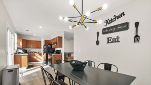 A modern kitchen with wooden cabinets, a black refrigerator, and a dining area with a dark table and chairs. - The ATL Escape (Atlanta)