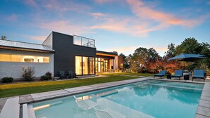 Uma casa moderna com piscina, área de estar externa e gramado bem cuidado.