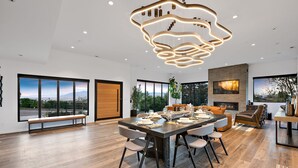 Uma sala de jantar espaçosa com um lustre moderno, amplas janelas com vista para o exterior e uma lareira.