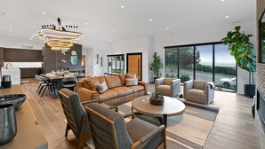 Interior moderno com sofá de couro, área de refeições e amplas janelas com vista.