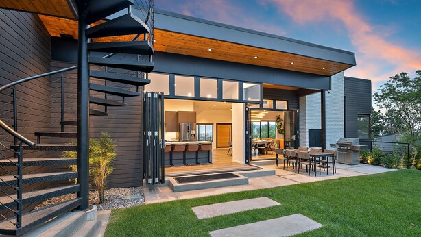 Uma casa moderna com uma escadaria em espiral, um pátio com mobiliário externo e um gramado bem cuidado.