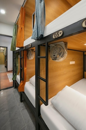 Quarto com beliches numerados e um ventilador em cada beliche.