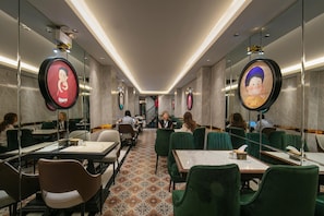 Um saguão de hotel com uma escadaria central, cadeiras estofadas em verde e piso estampado.