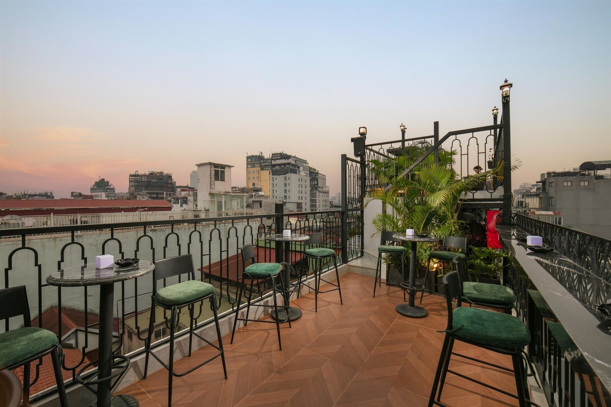 Una terraza en la azotea con mobiliario exterior, vistas de la ciudad y una barandilla de hierro decorativa.