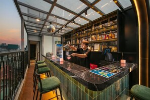 A bar area with a bartender preparing a drink, a high ceiling with a glass structure, and a city view.