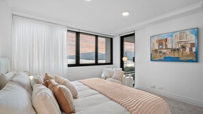 A bedroom with a bed, a window with a view of mountains, and a painting on the wall. - Luxury Oceanview Penthouse at Northshore Tower Cairns (Cairns North)