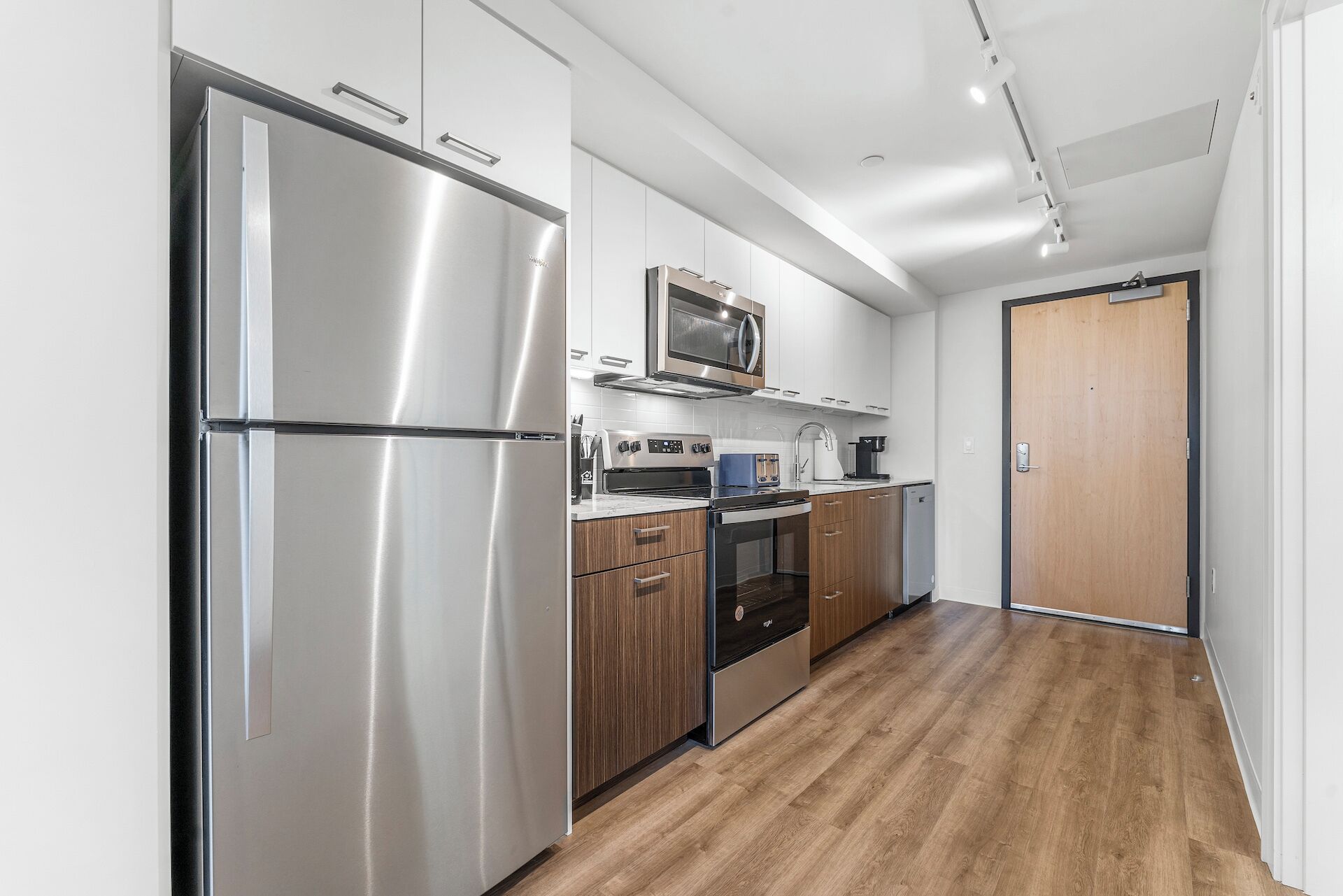 A modern kitchen with stainless steel appliances, wooden cabinets, and a wooden floor.