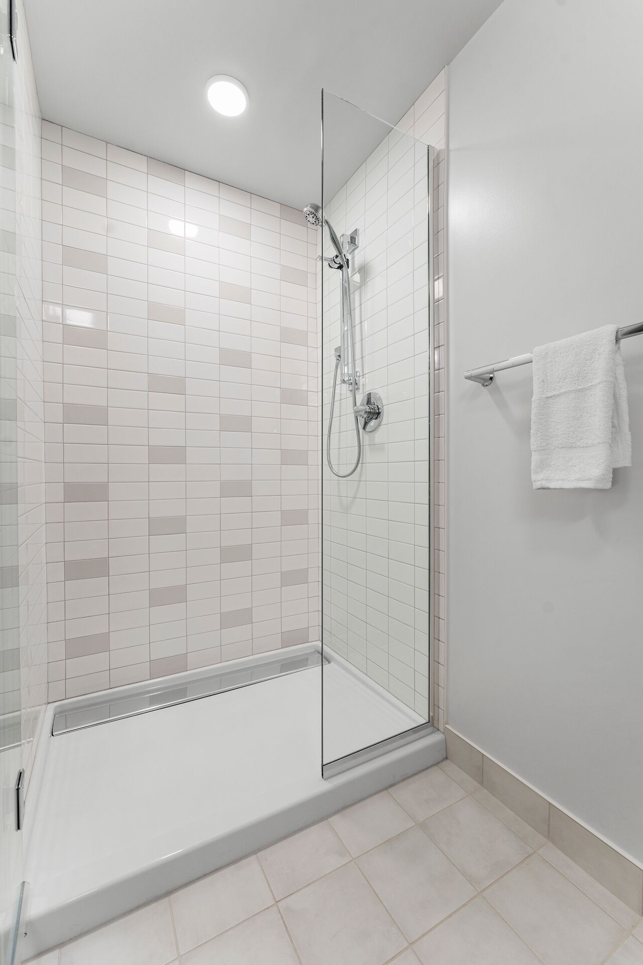 Une douche moderne avec une porte en verre, des murs recouverts de carreaux blancs et une serviette blanche posée sur un porte-serviettes.