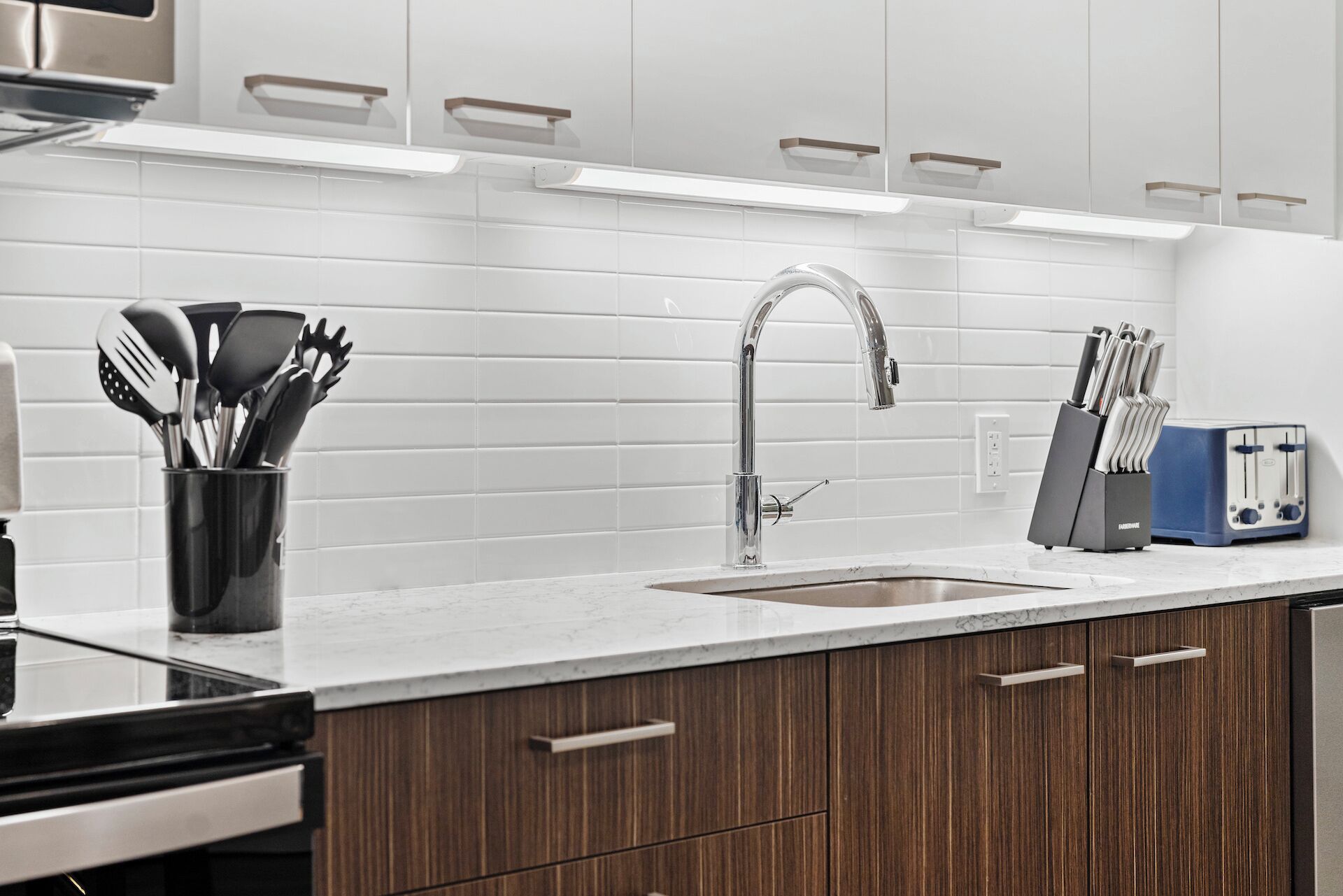 A modern kitchen with white subway tiles, a stainless steel faucet, wooden cabinets, and a built-in toaster.