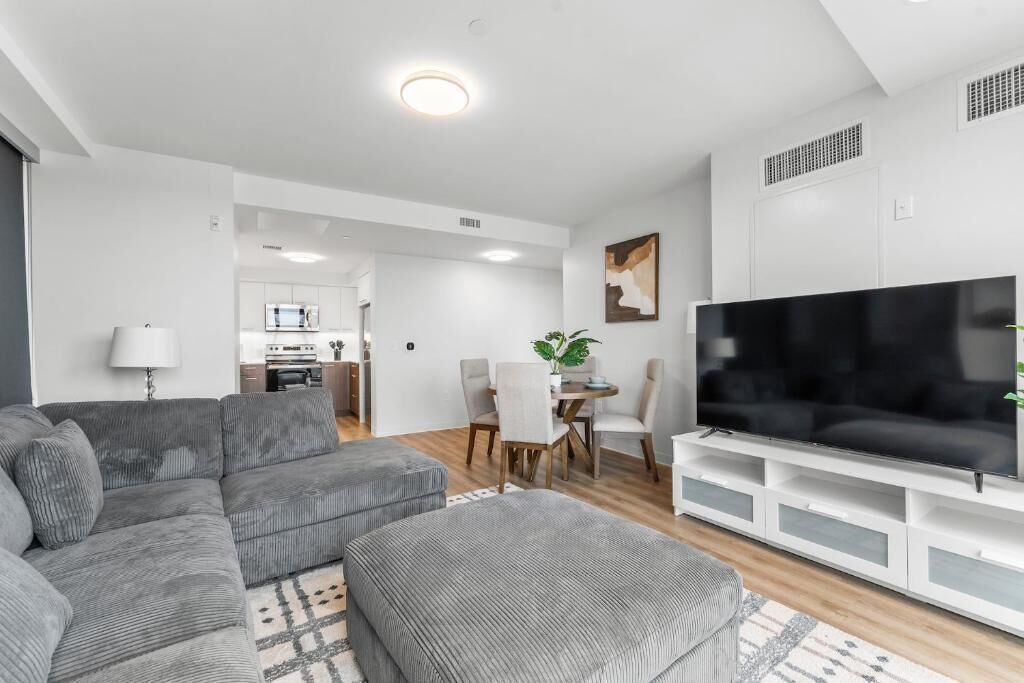 Un salon moderne avec un canapé d’angle gris, un téléviseur à écran plat et un coin repas comprenant une table et des chaises.