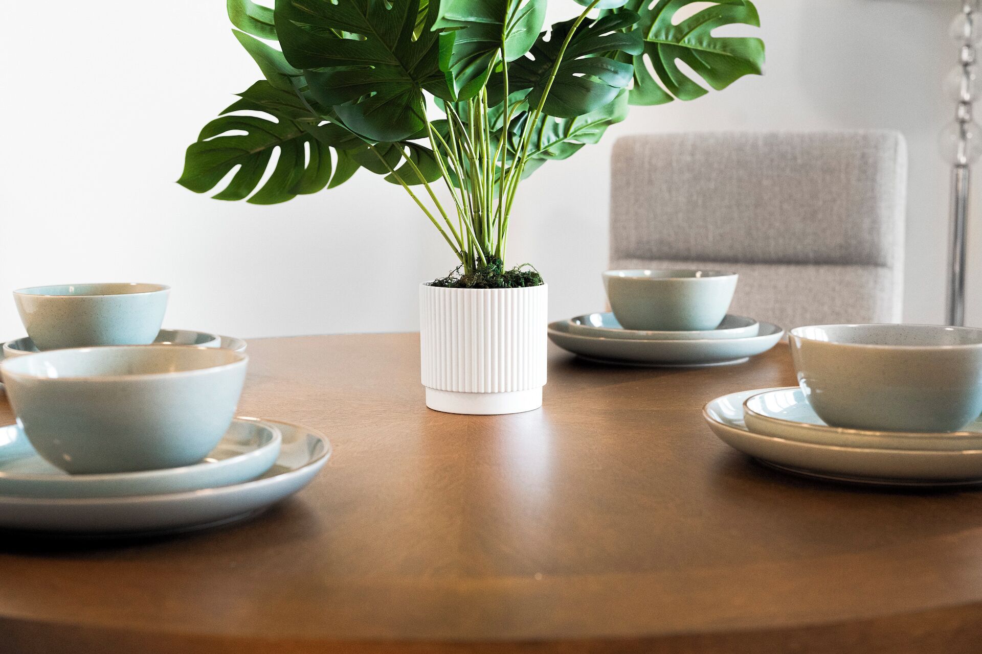 Un tavolo da pranzo con un vaso bianco a coste contenente verdeggianti foglie, circondato da ciotole e piattini in ceramica azzurra.