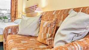 A cozy room with a patterned orange sofa, a wooden headboard, and a city view through a window with curtains. - Čertovka by Interhome (Harrachov)