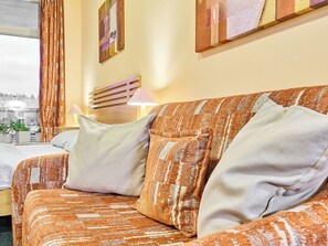 Ein gemütliches Zimmer mit einem orangefarbenen, gemusterten Sofa, einem hölzernen Kopfteil und Blick auf die Stadt durch ein mit Vorhängen drapiertes Fenster.