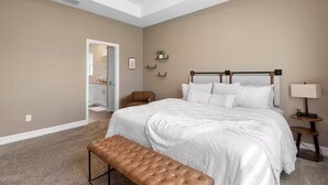 Een slaapkamer met een groot bed, een bankje, een nachtkastje en een wandplank.