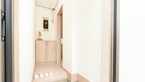 A narrow hallway with a wooden cabinet, a small table with a vase, and a pair of shoes on the floor. - Air Station Front Stay (Izumisano)