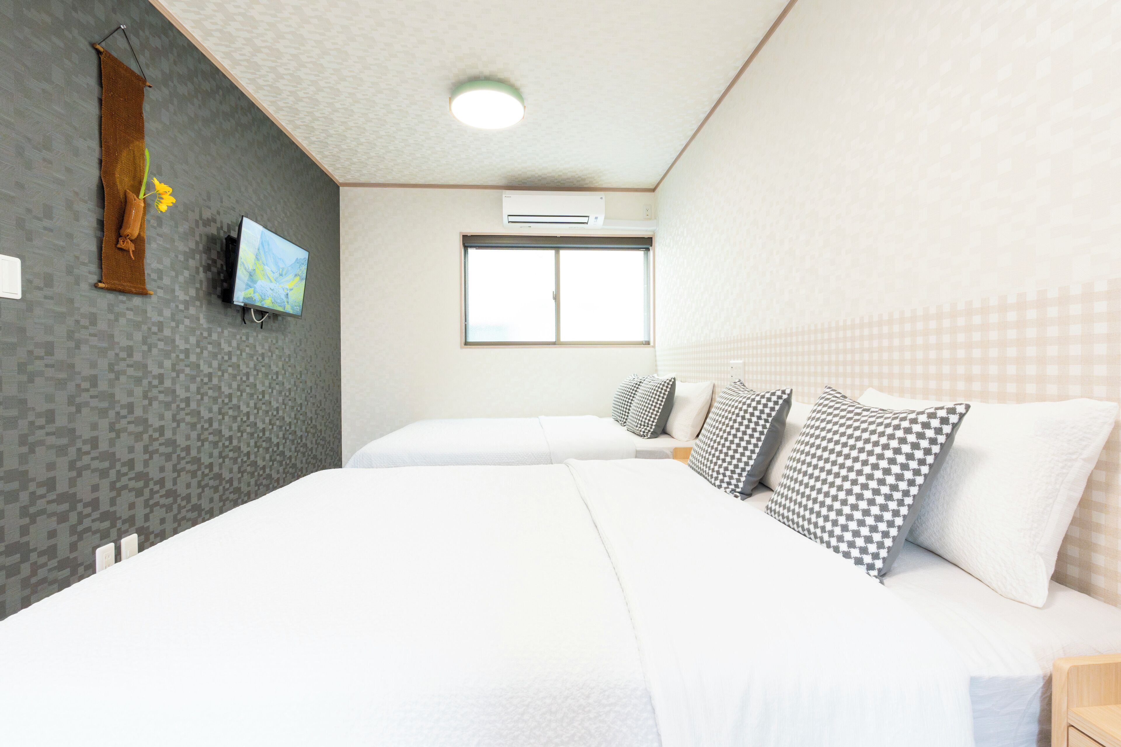 Habitación de hotel con dos camas, un televisor de pantalla plana, un equipo de aire acondicionado y una ventana.