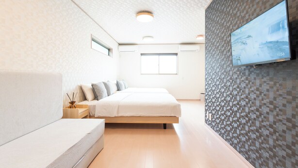 A modern bedroom with a bed, a sofa, a TV on the wall, and a window. - Air Station Front Stay (Izumisano)