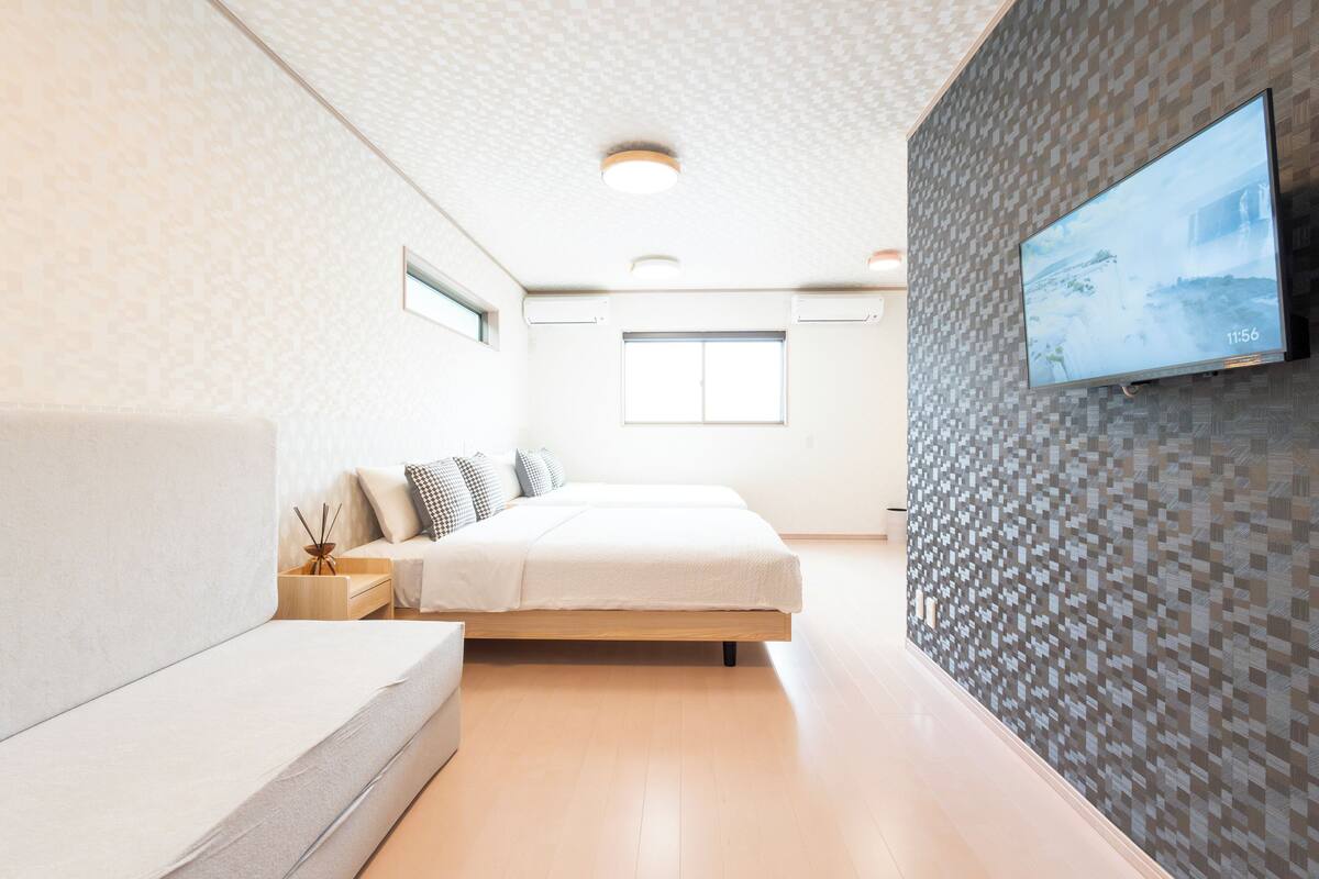 A modern bedroom with a bed, a sofa, a TV on the wall, and a window.