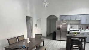 Een moderne keuken met een koelkast, fornuis en kastjes. Er staat een eettafel met stoelen en een bankje.
