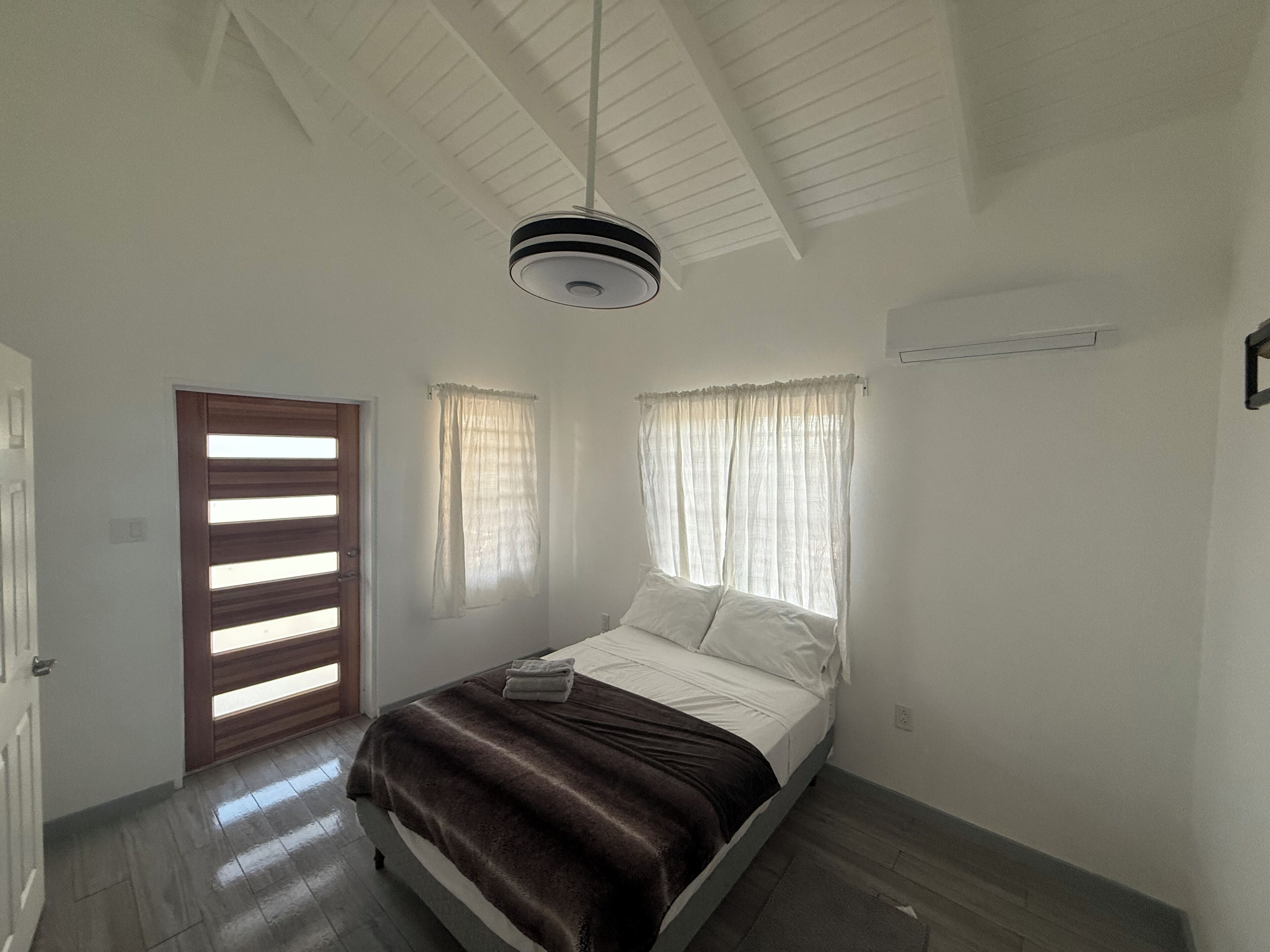 A bedroom with a bed, a ceiling fan, a door, and two windows with curtains.