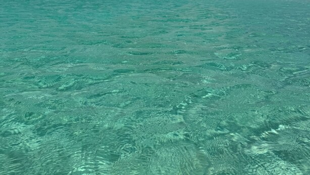Helder turquoise water met een zandstrand en een verre kustlijn.