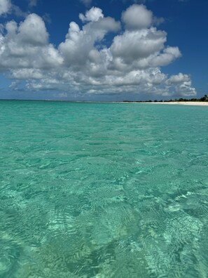 Une mer d’un bleu turquoise limpide, une plage de sable et une côte lointaine.