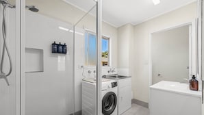 Un bagno moderno con box doccia in vetro, lavatrice a incasso, lavandino e specchio.