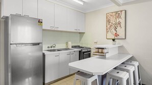 Una cucina funzionale con mobili bianchi, un frigorifero in acciaio inox, un fornello a gas e un piano di lavoro bianco con sgabelli.