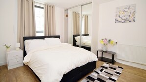 Un dormitorio moderno con una cama tapizada en negro, una mesita de noche con lámpara, un tocador y un radiador.