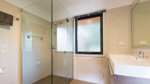 A modern bathroom with a glass shower enclosure, a large sink, and a window above the mirror.