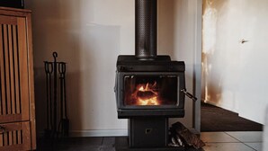 A wood-burning stove with a visible fire, a metal chimney, and a tiled floor.