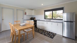 A modern kitchen with white cabinets, a stainless steel refrigerator, and a dining area with a wooden table and chairs.