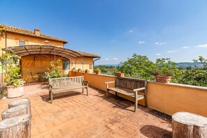 Eine Terrasse mit einer Holzbank, Blumentöpfen und Blick auf die Landschaft.