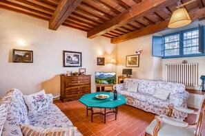 A cozy living room with wooden beams, a sofa, a chair, a table with a plate of food, and a TV. - Villa Salivolpe Amazing Chianti View 14, San Casciano VDP, Italy (San Casciano VDP)