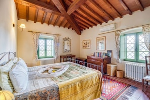 Um quarto aconchegante com teto de madeira, uma cama com colcha florida, uma escrivaninha pequena e uma janela com cortinas.