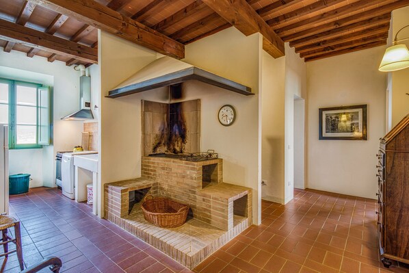 Una cocina rústica con chimenea de ladrillo, vigas de madera y un reloj en la pared.