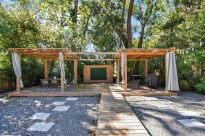 A wooden pergola structure with a seating area and a green wall, surrounded by gravel and trees. - Downtown Jacksonville Retreat | Pet-Friendly with Hot Tub & Backyard Oasis (Jacksonville)
