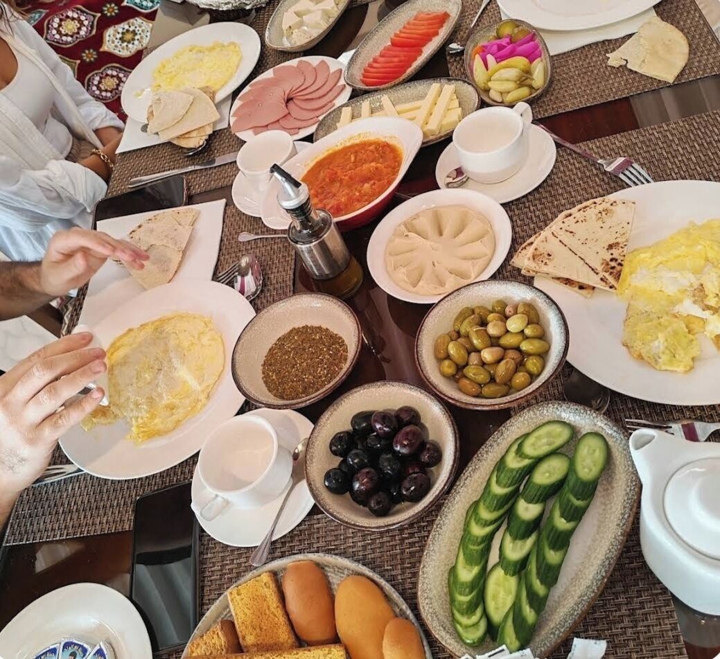 A breakfast buffet with various dishes including eggs, meats, olives, and bread.