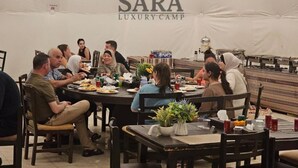 Un groupe de personnes est assis à une table dans une tente, et le logo « SARA LUXURY CAMP » est visible sur un des murs.