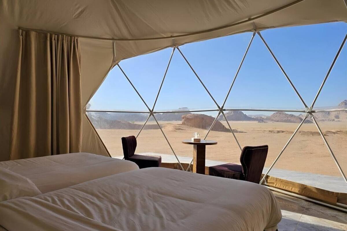 Une pièce aménagée avec une tente, comprenant un lit, deux chaises et une petite table, et offrant une vue sur un paysage désertique.