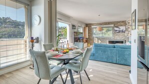 Ein moderner Essbereich mit einem für vier Personen gedecktem Tisch, einem blauen Sofa im Hintergrund und einem durchgehenden Zugang zur Küche.