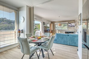 Ein moderner Essbereich mit einem für vier Personen gedecktem Tisch, einem blauen Sofa im Hintergrund und einem durchgehenden Zugang zur Küche.