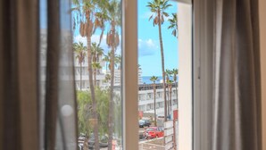 A view through a window with curtains, featuring palm trees, a parking lot, and a building with balconies. - Two-bedroom apartment with pool and tennis court (Costa Adeje)