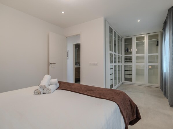 A bedroom with a bed, a bathroom visible through an open door, and a walk-in closet with glass doors.