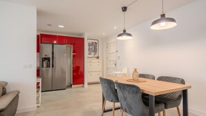 A modern kitchen with a stainless steel refrigerator, a red accent wall, and a dining area with a wooden table and grey upholstered chairs. - Two-bedroom apartment with pool and tennis court (Costa Adeje)